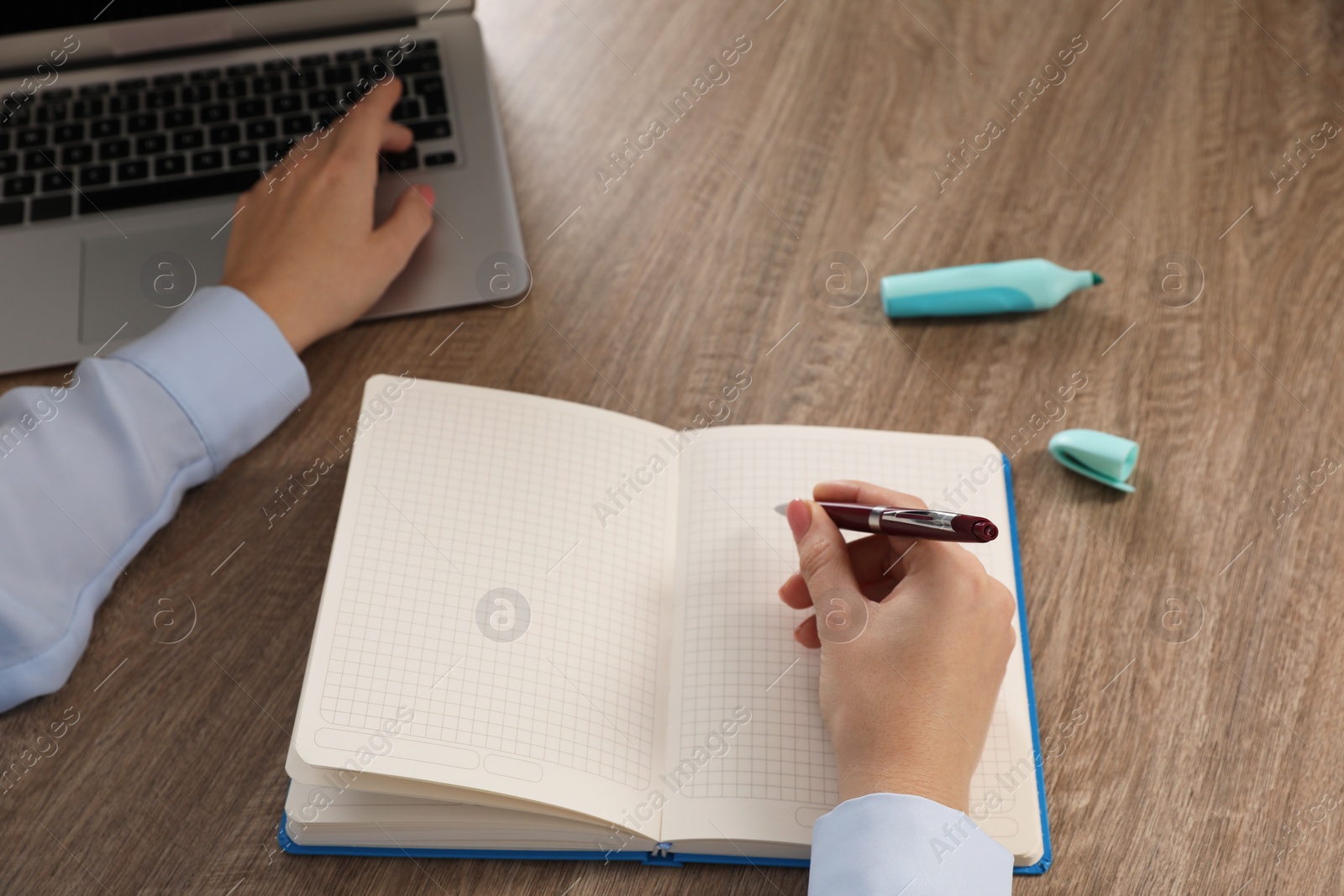 Photo of Woman taking notes while using laptop at wooden table, closeup