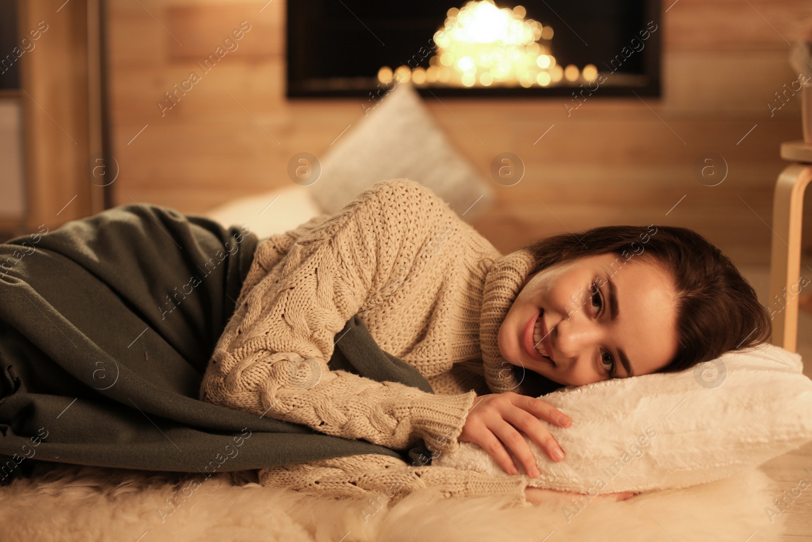 Photo of Young woman resting near decorative fireplace at home. Winter season