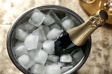 Photo of Bottle of champagne in bucket with ice cubes on table, view from above