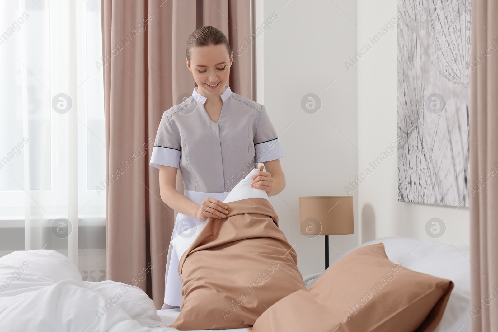 Photo of Young maid making bed in hotel room