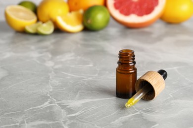 Bottle of essential oil with different citrus fruits on grey marble table. Space for text