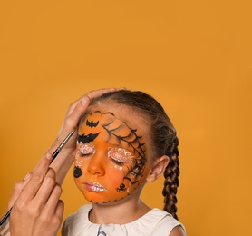 Photo of Artist painting face of little girl on orange background