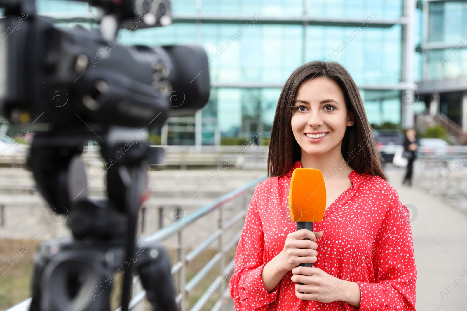 Photo of Young female journalist with microphone working on city street