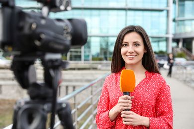 Photo of Young female journalist with microphone working on city street