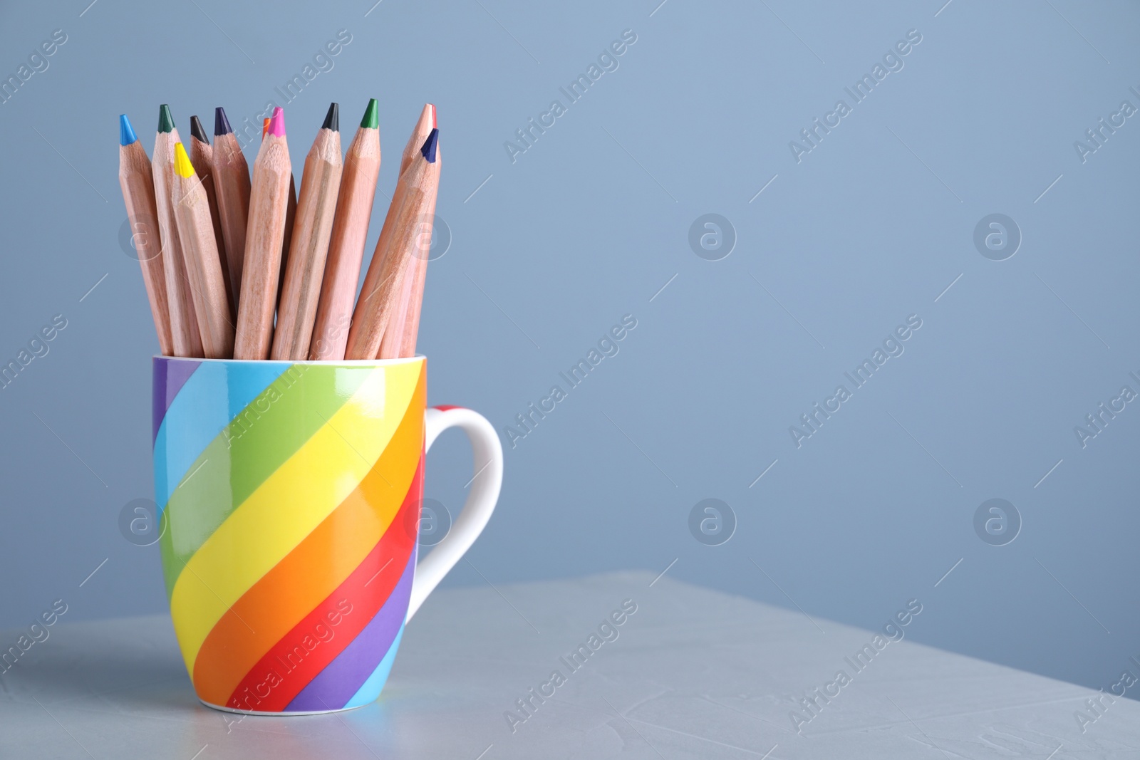 Photo of Colorful pencils in cup on grey table against light blue background. Space for text