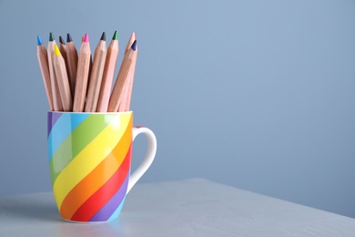 Colorful pencils in cup on grey table against light blue background. Space for text
