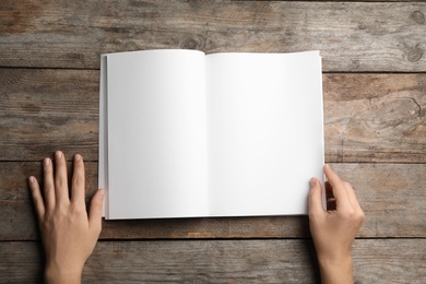 Woman holding brochure with blank pages on wooden background, top view. Mock up for design