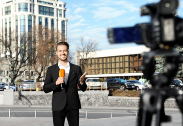 Young male journalist with microphone working on city street