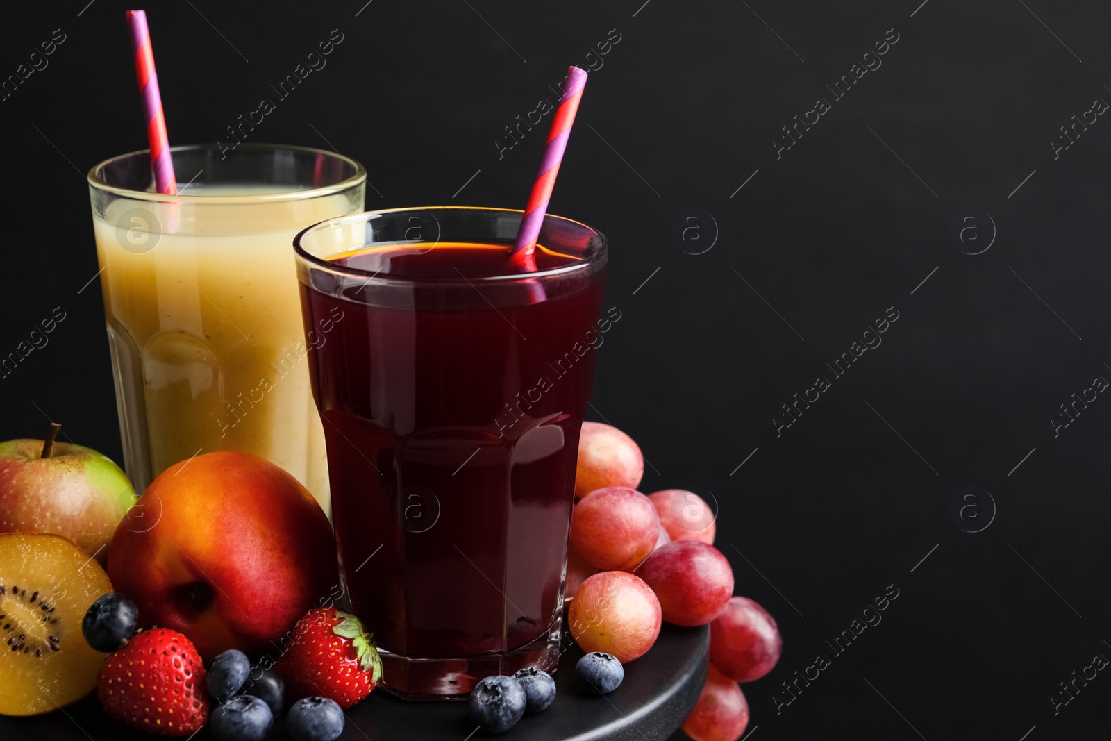 Photo of Delicious juices and fresh ingredients on table against black background. Space for text