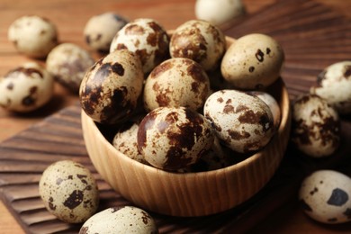 Photo of Bowl and many speckled quail eggs on table, closeup