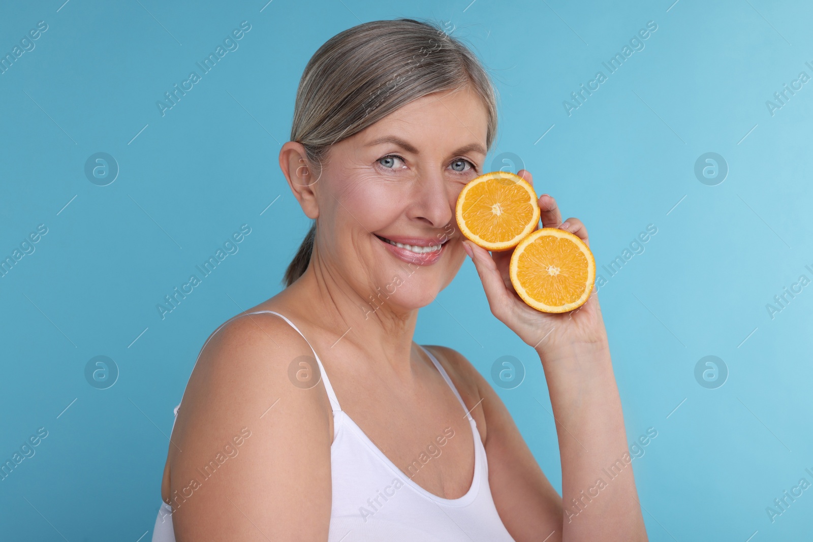 Photo of Beautiful woman with halves of orange rich in vitamin C on light blue background