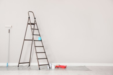 Photo of Decorator's tools and ladder near white wall indoors, space for text