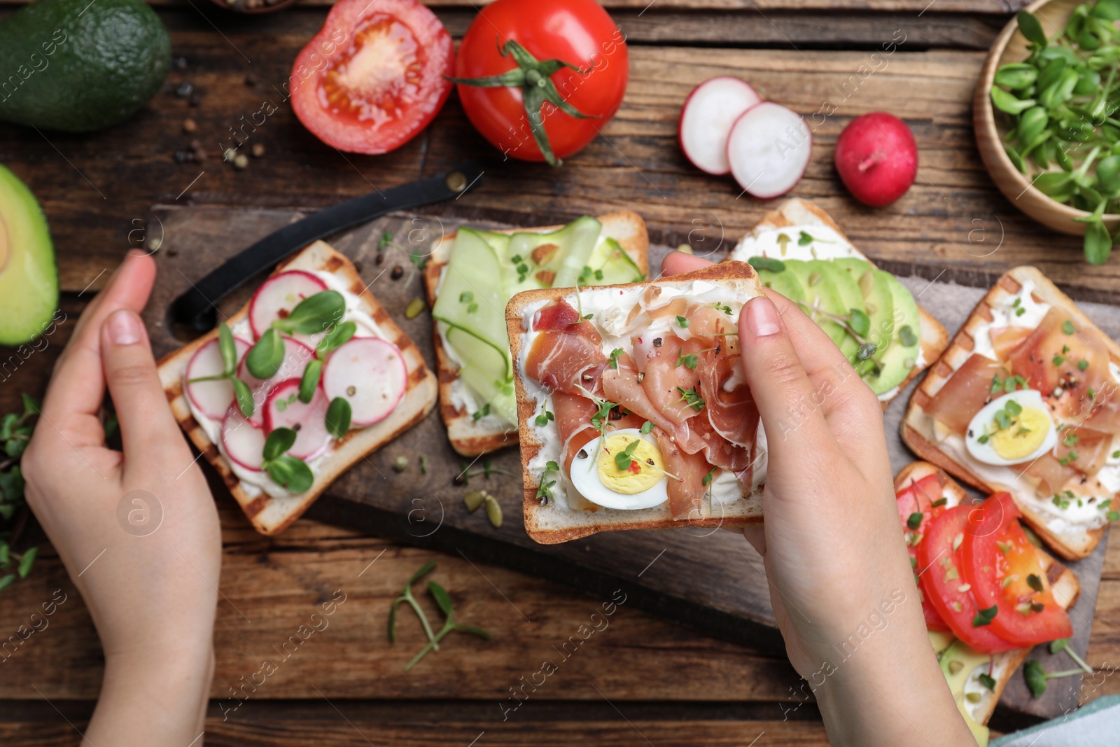 Photo of Woman cooking delicious sandwiches with microgreens at wooden table, top view