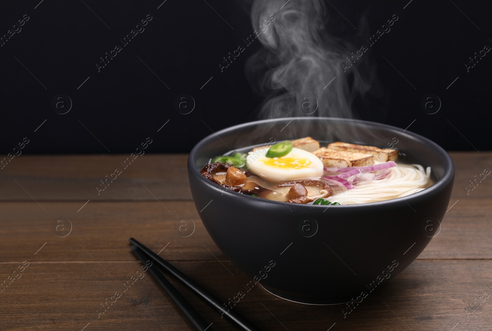 Image of Delicious hot vegetarian ramen in bowl on wooden table against black background, closeup. Space for text