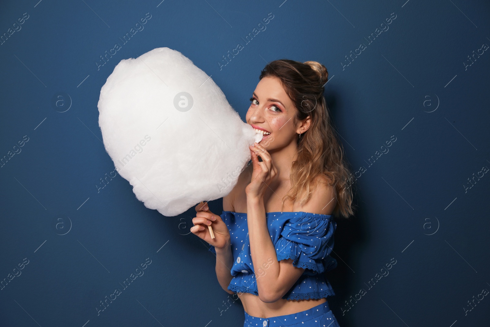 Photo of Portrait of young woman biting cotton candy on blue background