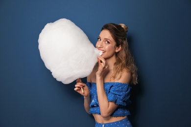 Portrait of young woman biting cotton candy on blue background