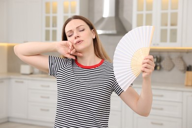 Woman with hand fan suffering from heat in kitchen