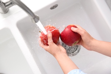 Woman washing fresh red apples in kitchen sink, top view