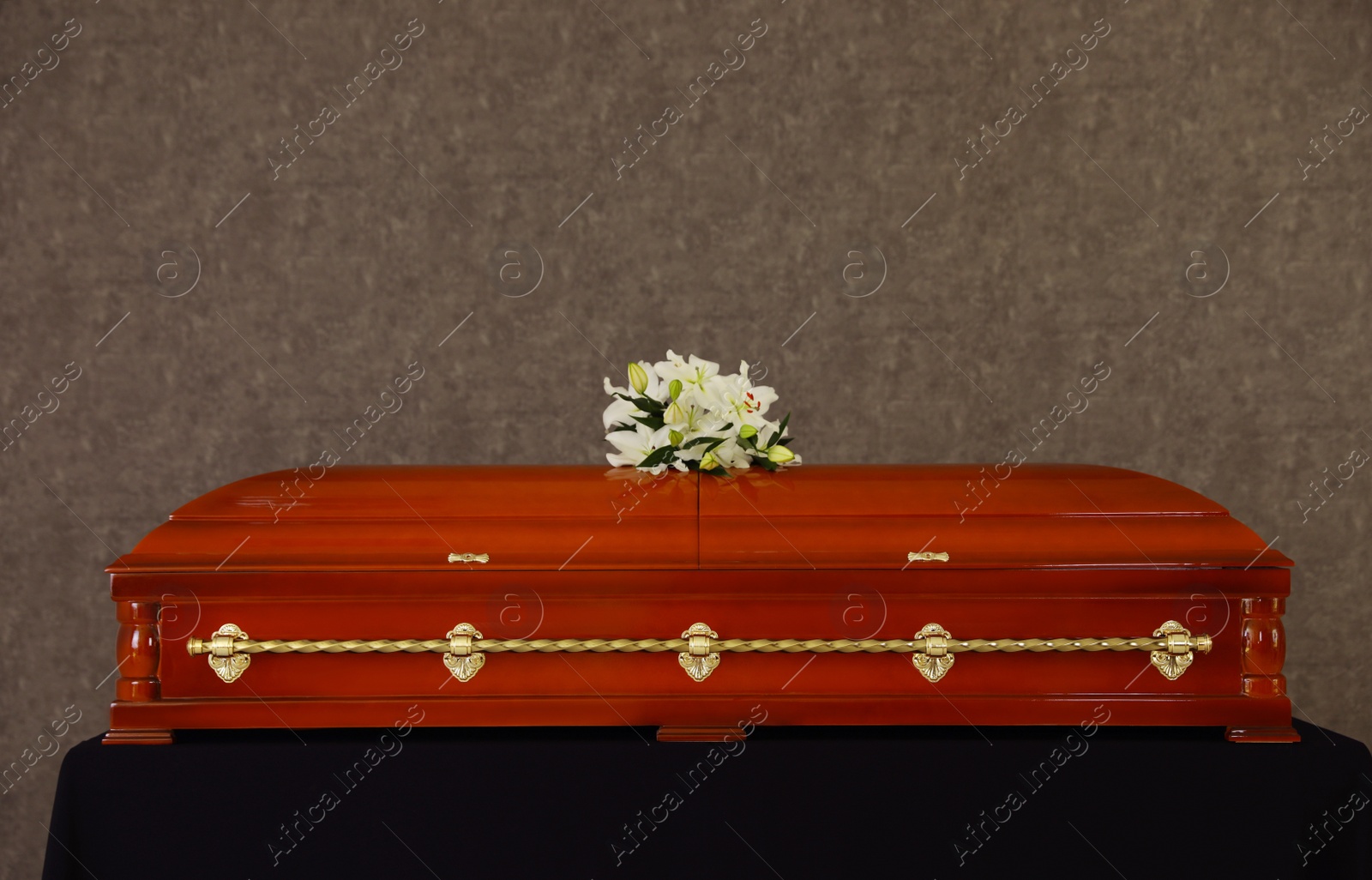 Photo of Wooden funeral casket with white lilies at grey wall