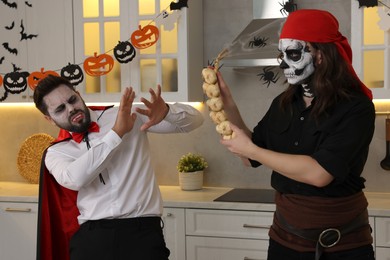 Photo of Skeleton pirate with garlic warding off scared vampire indoors. Halloween celebration