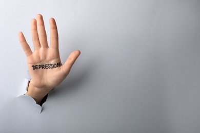 Photo of Woman showing hand with written word DEPRESSION through torn paper. Space for text