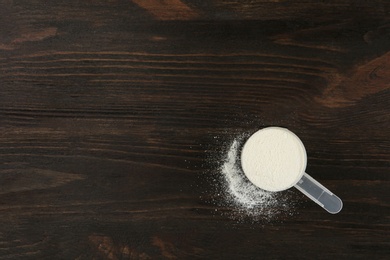 Photo of Measuring scoop of protein powder on wooden table, top view. Space for text