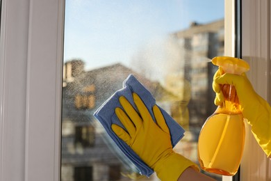 Photo of Young woman cleaning window glass with rag and detergent at home, closeup