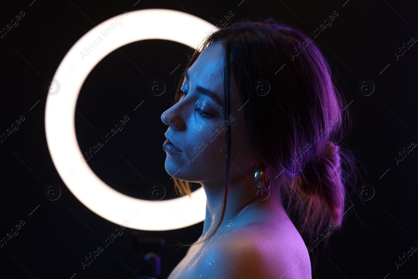 Photo of Beautiful woman and ring lamp on dark background in neon lights