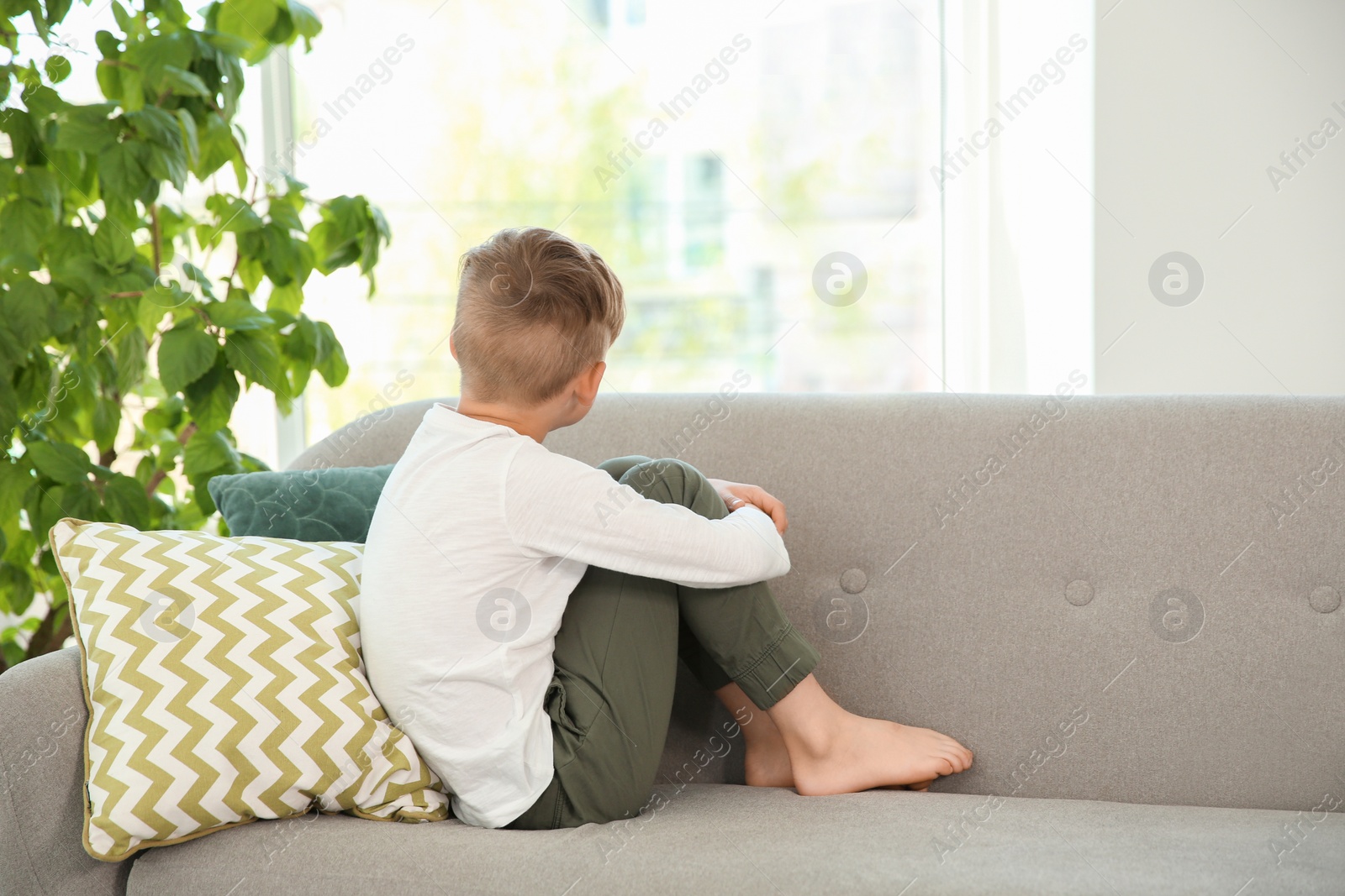 Photo of Lonely little boy sitting on couch at home. Autism concept