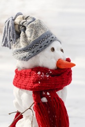 Photo of Funny snowman with scarf and hat in winter forest, closeup