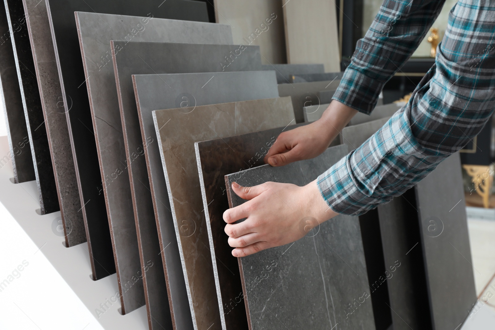 Photo of Man choosing tile among different samples in store, closeup