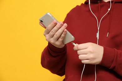 Photo of Man plugging earphones to smartphone on yellow background, closeup. Space for text