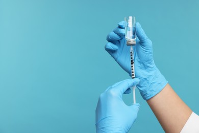 Photo of Doctor filling syringe with medication from glass vial on light blue background, closeup. Space for text