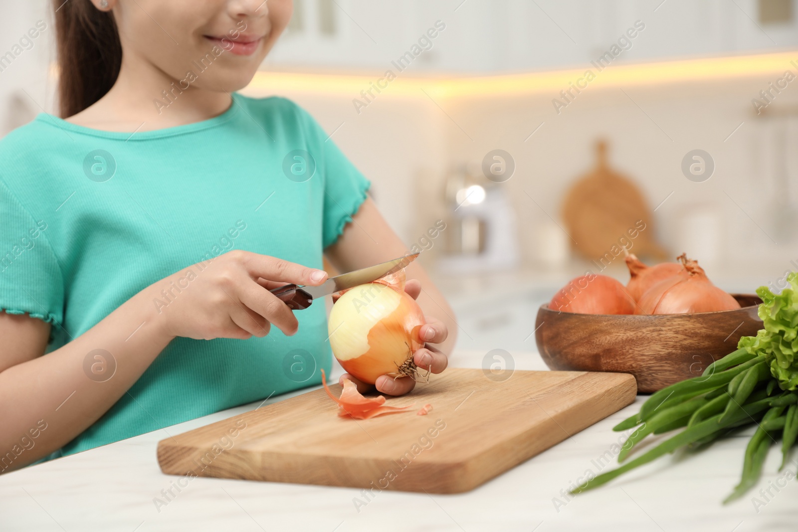 Photo of Child peeling fresh vegetable at table in kitchen, closeup