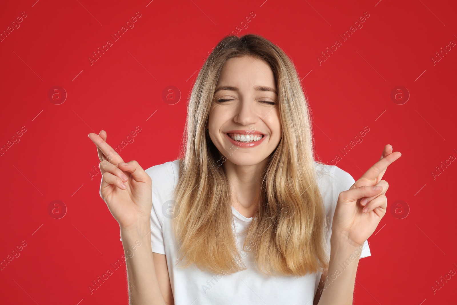 Photo of Woman with crossed fingers on red background. Superstition concept