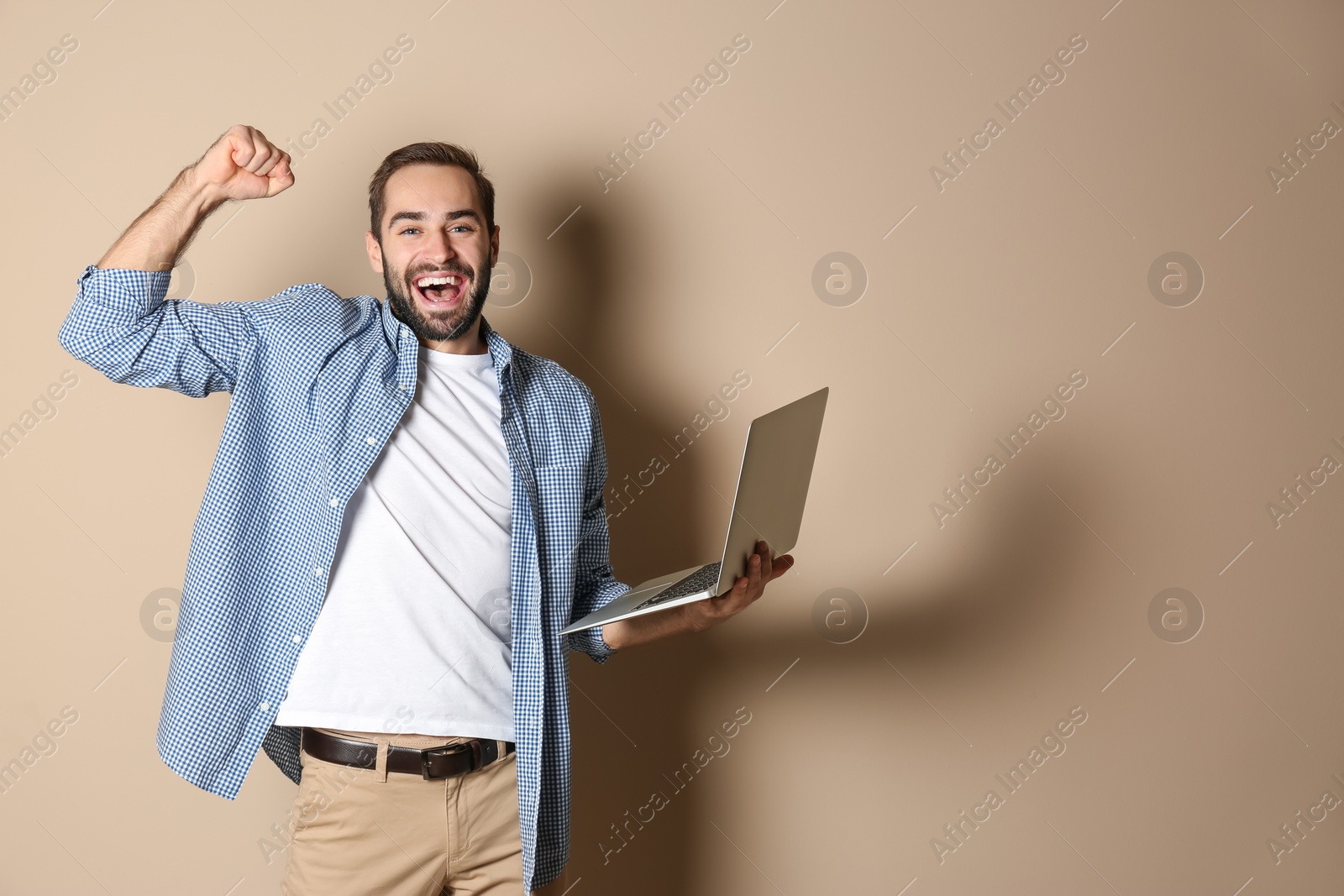 Photo of Emotional young man with laptop celebrating victory on color background. Space for text