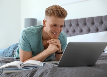 Photo of Young man using laptop while lying on bed at home