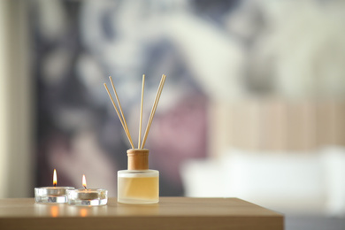 Aromatic reed air freshener and scented candles on table indoors. Space for text