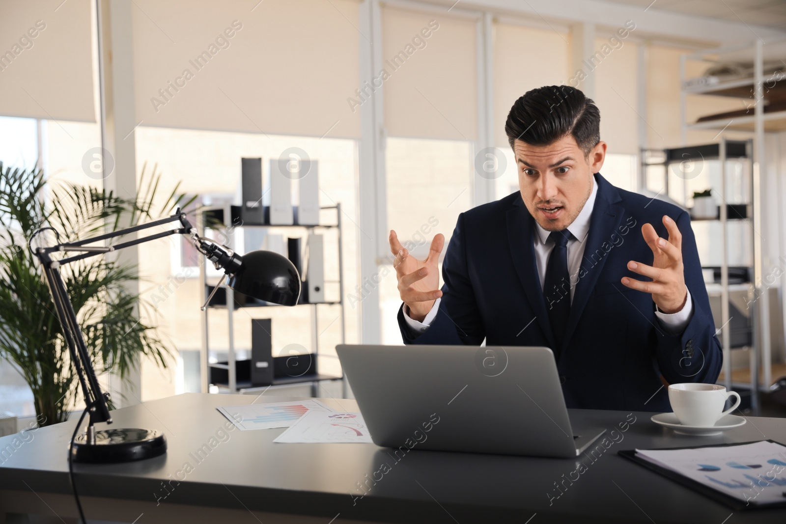 Photo of Emotional businessman with laptop at table in office