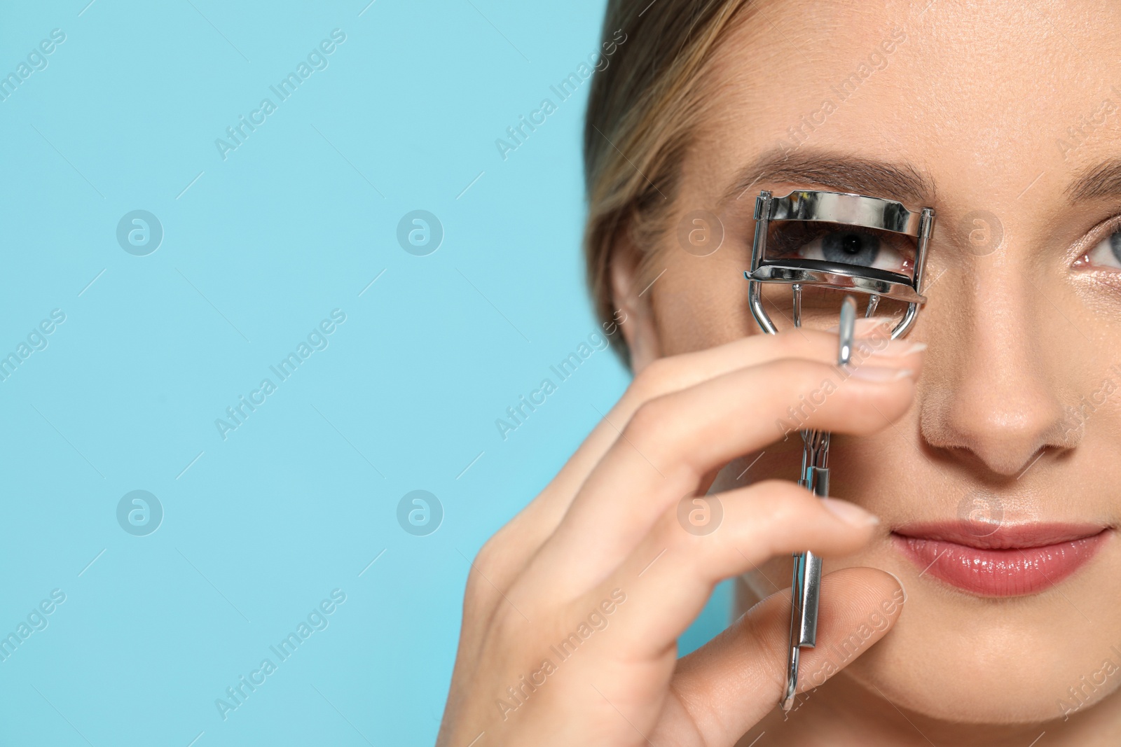 Photo of Young woman using eyelash curler on light blue background, closeup. Space for text