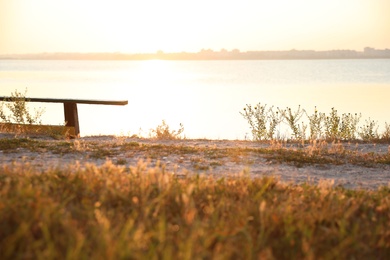 Photo of Wooden bench near river at sunrise. Early morning landscape