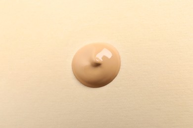 Drop of skin foundation on beige background, top view