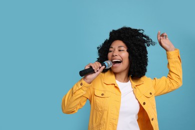 Beautiful woman with microphone singing on light blue background, space for text