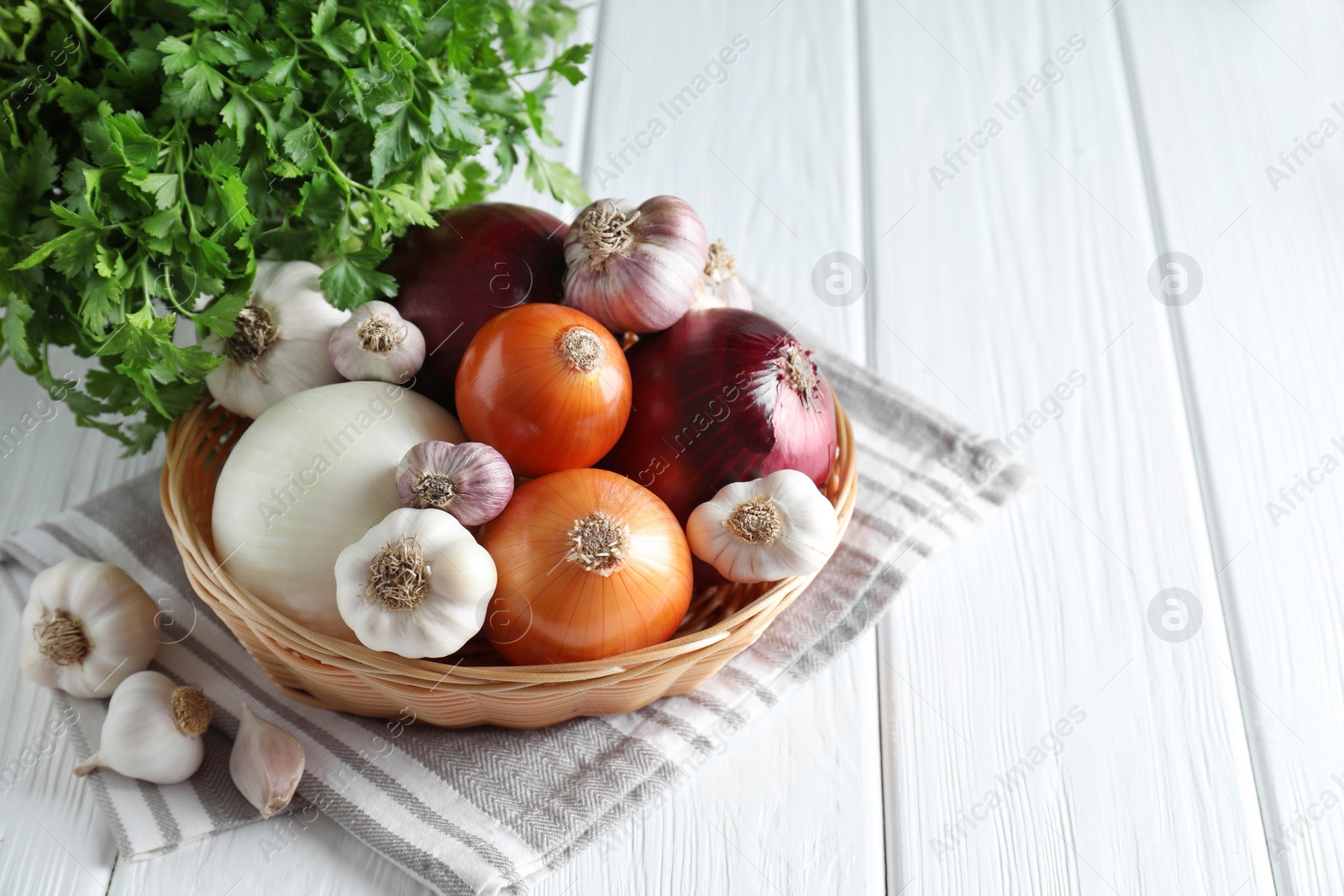 Photo of Fresh raw garlic, onions and parsley on white wooden table. Space for text