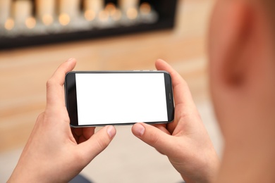 Man holding smartphone with blank screen indoors, closeup of hands. Space for text