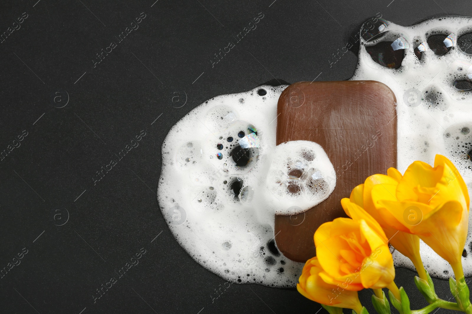 Photo of Flat lay composition with flowers, soap bar and foam on black background. Space for text