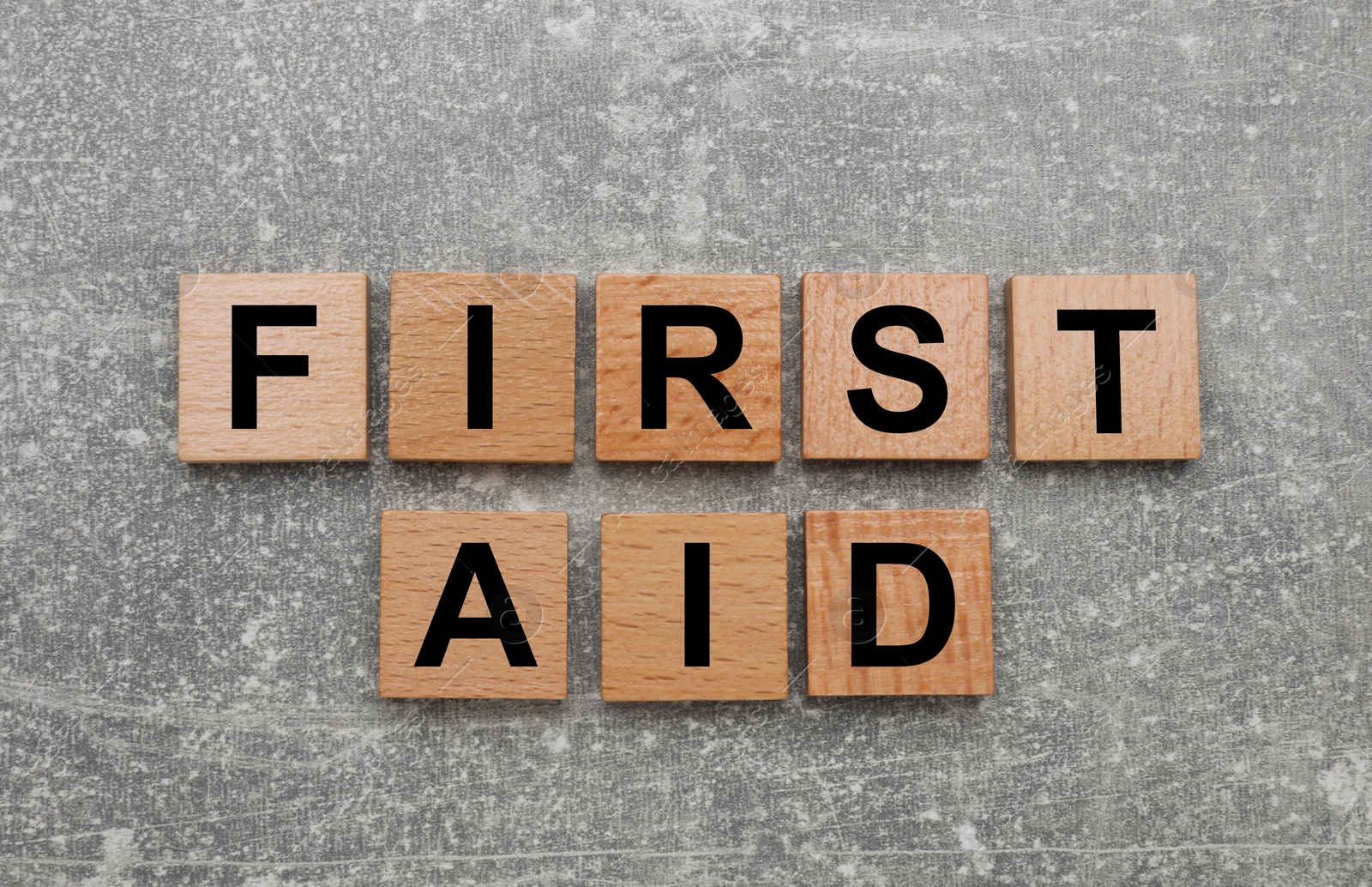 Photo of Words First Aid made of wooden cubes on light grey table, flat lay