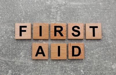 Photo of Words First Aid made of wooden cubes on light grey table, flat lay