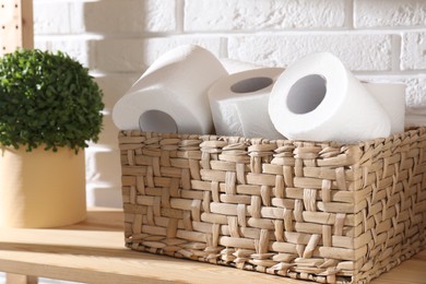 Photo of Toilet paper rolls in wicker basket and floral decor on wooden shelf near white brick wall