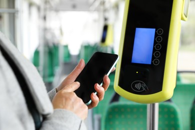 Photo of Woman with smartphone near contactless fare payment device in public transport, closeup